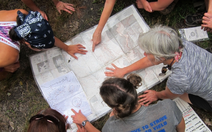 a group of people examine a map that is spread out on the ground